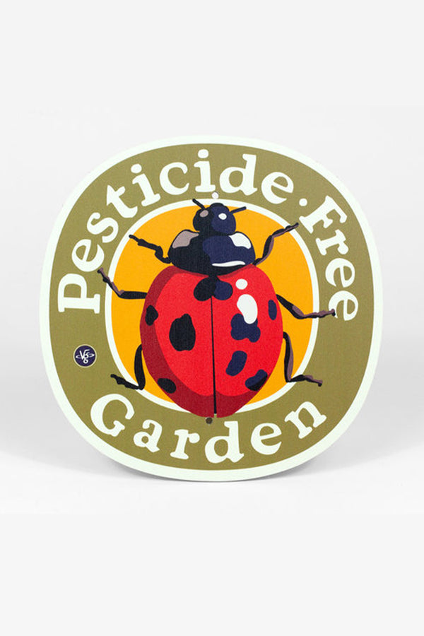 A round metal garden sign sits on a white background. The sign is has an olive green border with text that reads "Pesticide Free Garden" and has an illustration of a ladybug.