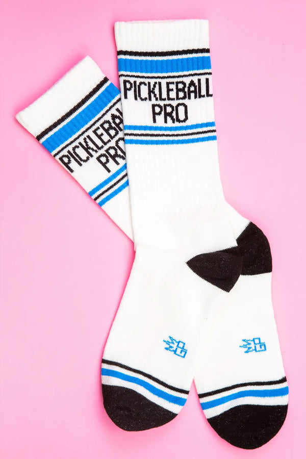 White mid-calf socks with a black heel and toe. Across the toe is a blue stripe with a thin black stripe above it. Across the top of the socks are black and blue stripes and in between them the socks say Pickleball Pro in black lettering. Pink background.