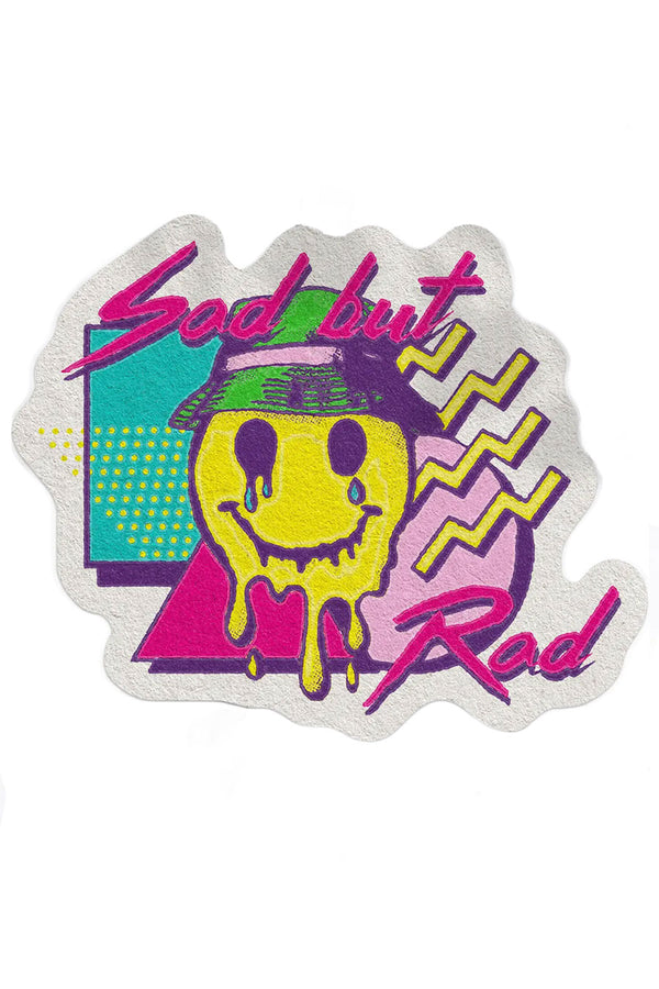 White sticker on a white background. Sticker features a melted smiley face wearing a bucket hat surrounded by various 90's style shapes in Aqua, purple, pink, and yellow. The sticker says Sad But Rad.