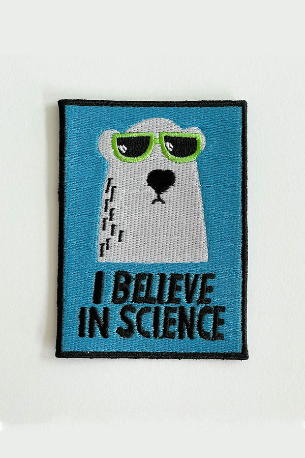 A vertical rectangular embroidered patch depicting an illustrated polar bear wearing green sunglasses. The text reads "I believe in science." The patch is light blue with black lettering and a black border.