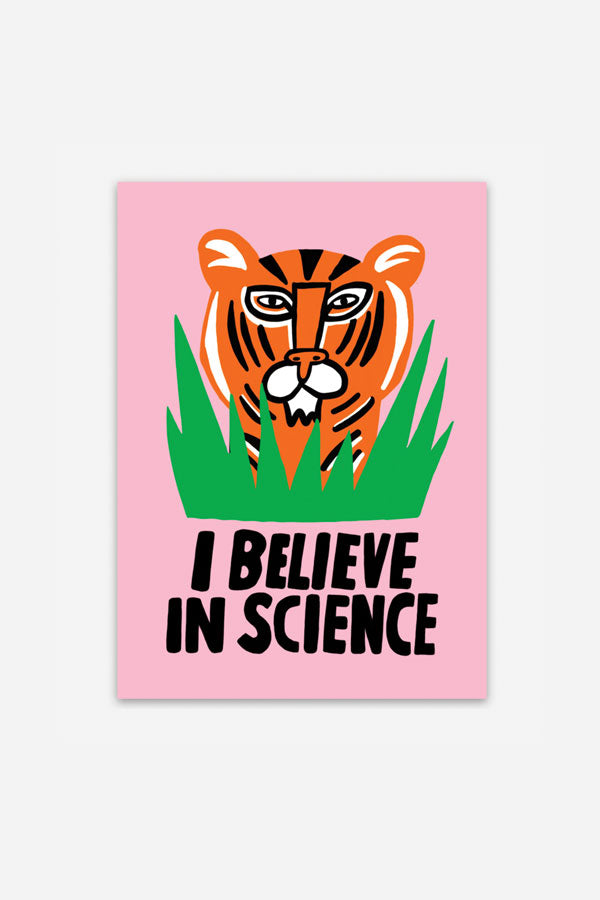 A vertical rectangular sticker with black text that reads "I believe in science." The sticker is light pink with an illustration of an orange tiger's head hiding in tall blades of green grass.