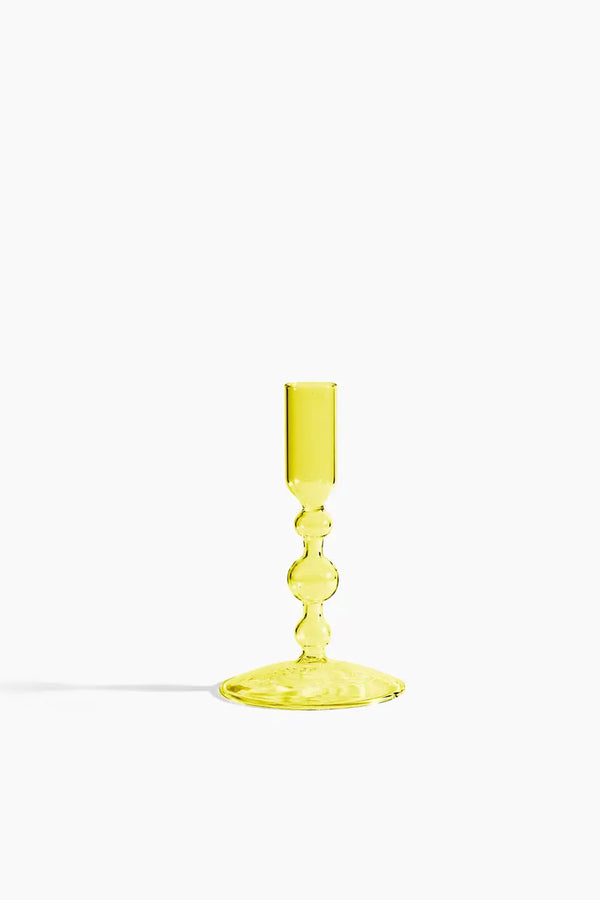 Short yellow glass votive candle holder against a white backdrop.