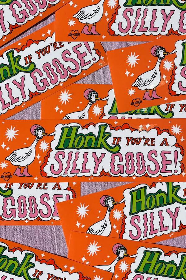 Multiple orange bumper stickers laying on top of one another on a pink linen background. The sticker features a white goose illustration wearing a pink bonnet. The goose has a text bubble coming from its beak that says "Honk if you're a silly goose!" The text is in Green, red, and pink text.