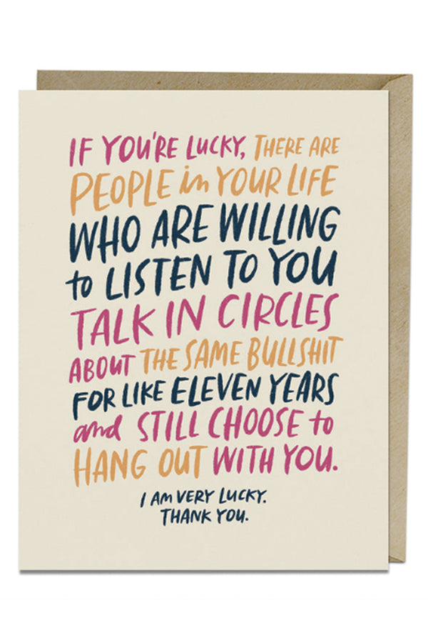 Off white greeting card with kraft brown envelope on white background. The card says "If your'e luck, there are people in your life who are willing to listen to you talk in circles about the same bullshit for like eleven years and still choose to hang out with you. I am very lucky. Thank you." The text is in Pink, Yellow, and navy blue colors.